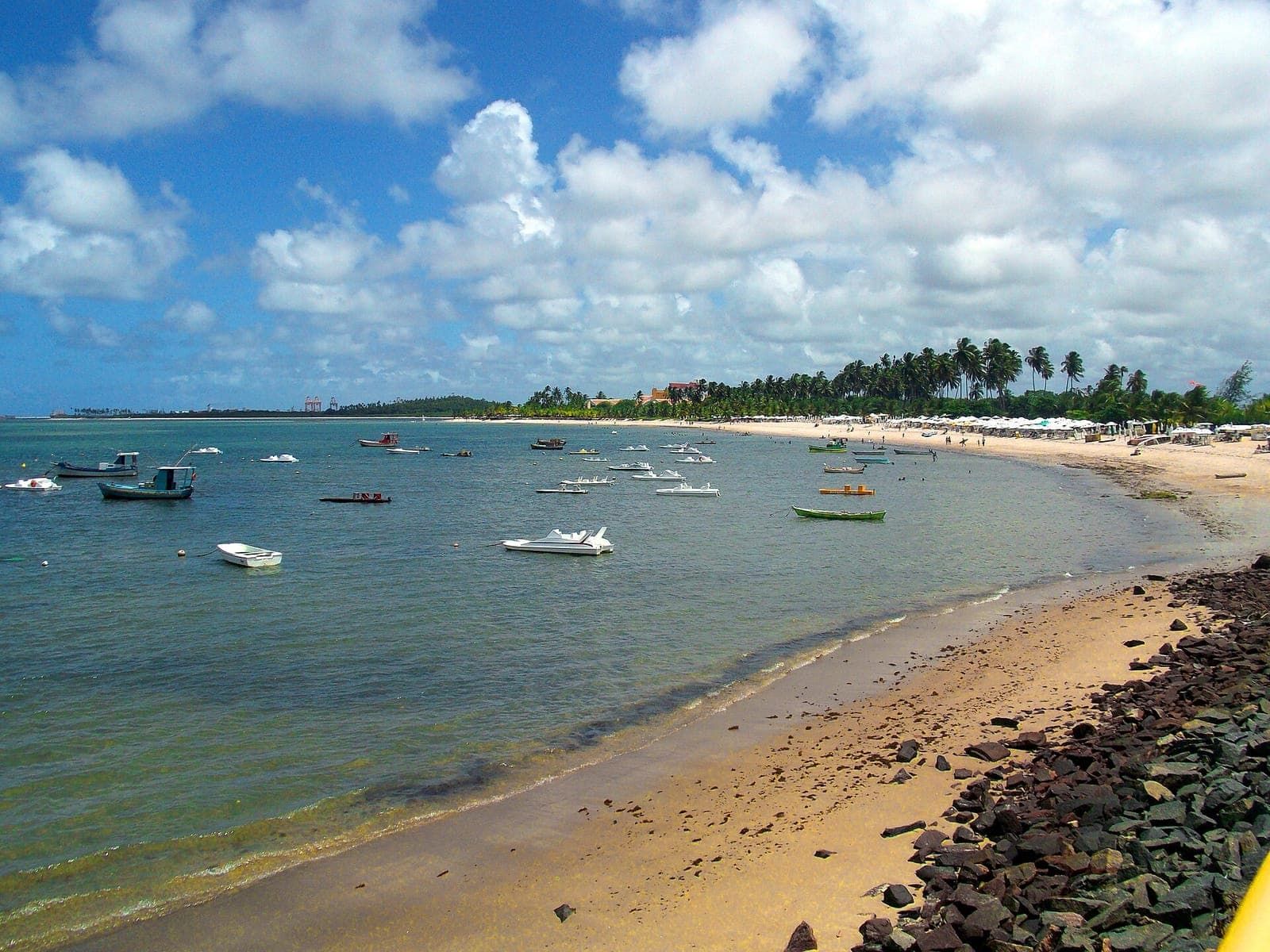 Praia de Suape com mar calmo e raso, barcos ancorados e coqueiral ao fundo